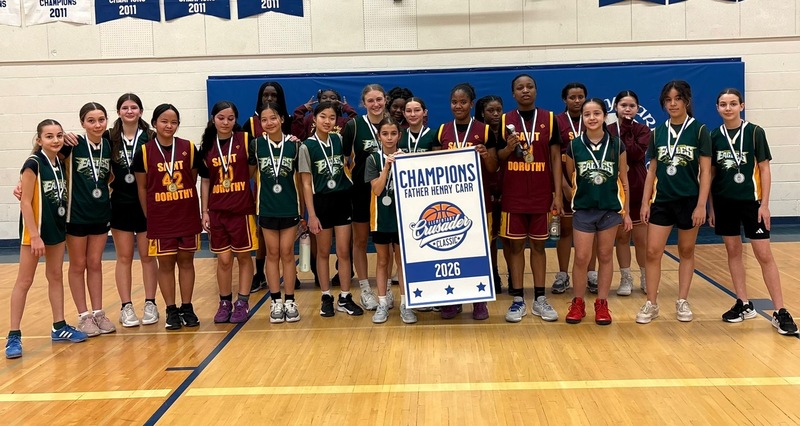 A girls basketball team photo in the gym, holding up a Champions 2026 banner