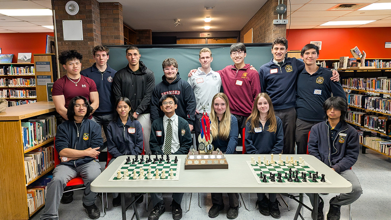 Photo of students at the tournament posing together with chess boards and awards