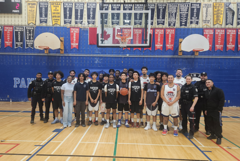 Large group photo - boys basketball team posing with police officers in a gym. 