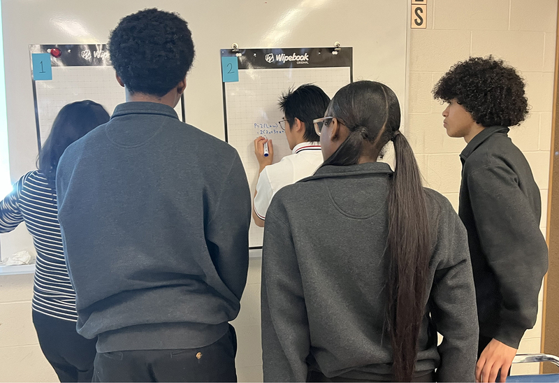 Photo of students working on math sums together on the board