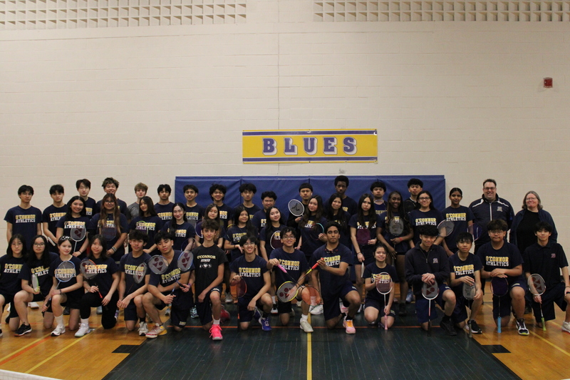 Large group photo of badminton team in a gym.
