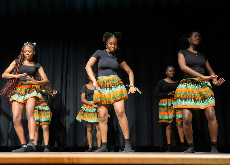 Photo of MPJ students performing a dance on stage while wearing colourful skirts with traditional African patterns