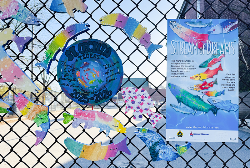 Photo of the colored wooden fish placed along the school fence along with a poster explaining Stream of Dreams