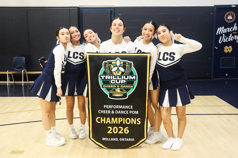 Photo of the Loretto College School Lightning Pom team posing with their championship banner