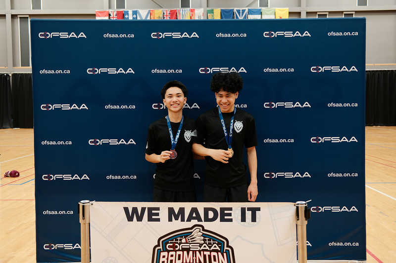 Photo of Frank and Neilan posing with their medals in front of an OFSAA board