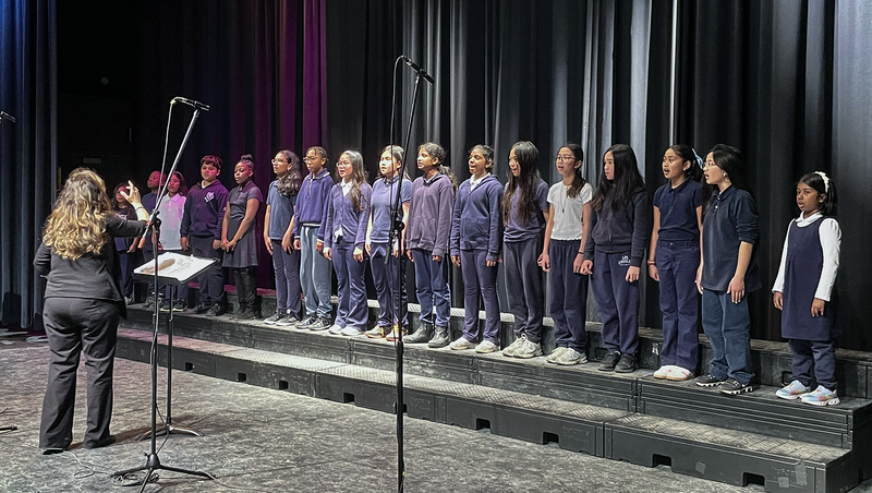 Photo of teacher conducting TCDSB music students on the stage
