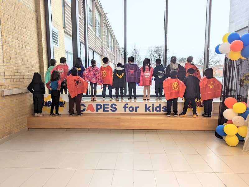 Group photo of St. Paschal Baylon students in superhero costumes looking out of a window