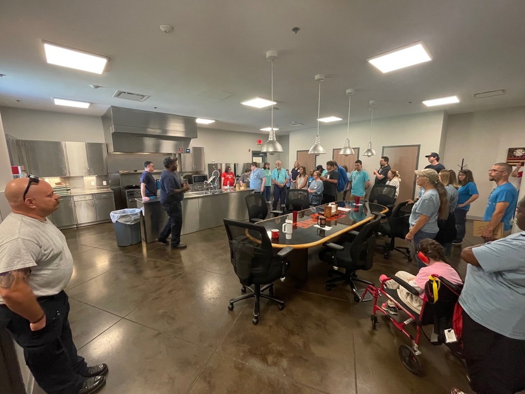 A group of adults gathered in a large, fire station kitchen listening to information from uniformed firefighters