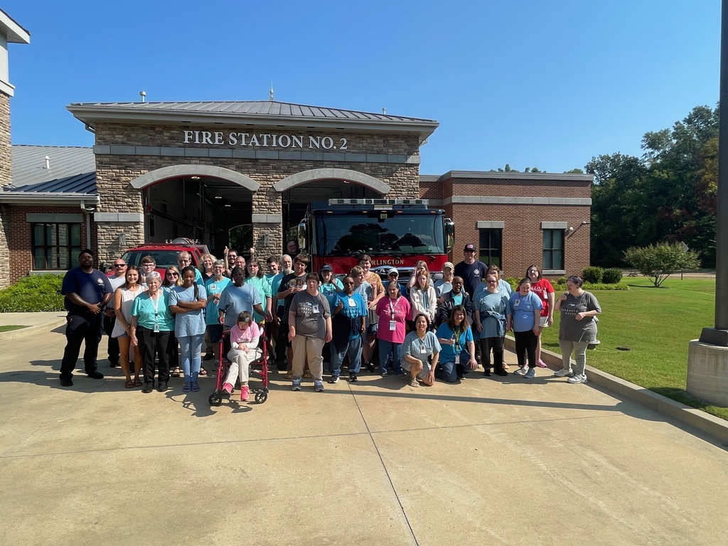 Large group of special needs adults posing with AFD members in front of Fire Trucks and a stone and brick building labeled as Fire Station No 2