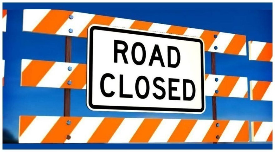 Orange and white road closed barrier with a bright blue sky in background