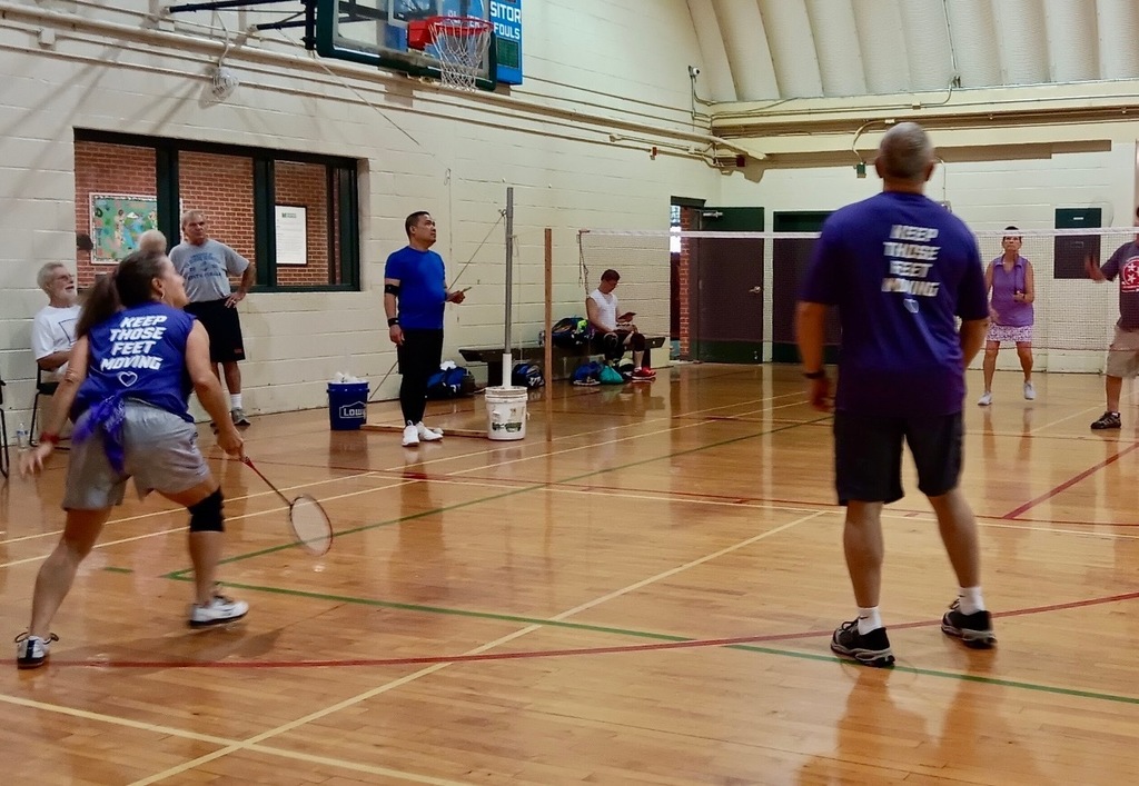 seniors in a gymnasium in the middle of a badminton game, one team wearing purple arlington shirts