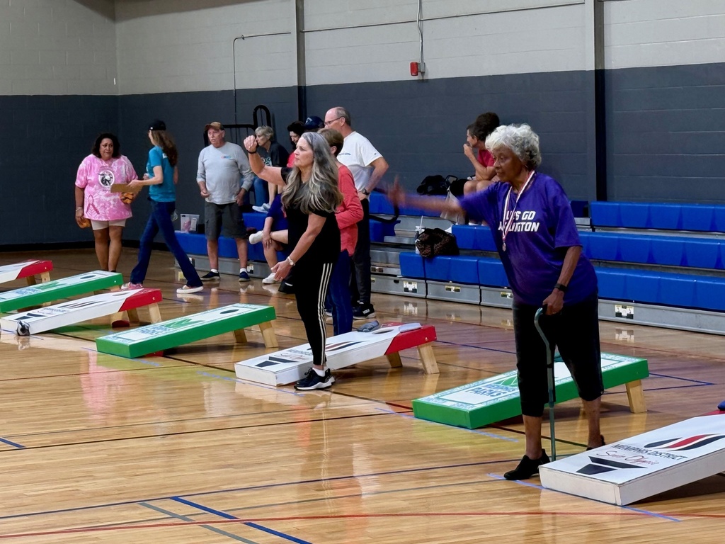 a line of senior women tossing cornhole bags in a gymnasium