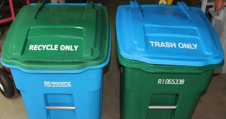 Picture of two large residential trash bins: one blue recycle bin with a green lid, and one green trash bin with a blue lid