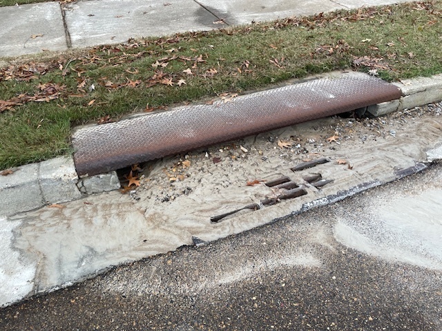 Picture of storm drain inlet filled with mud and rocks on side of a roadway