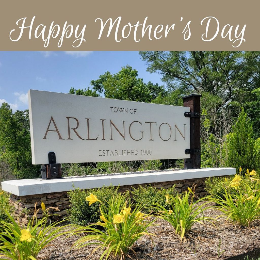 Photo of a town of arlington monument sign surrounded by yellow flowers and a blue sky in background. Text on top says Happy Mother's Day in white. 