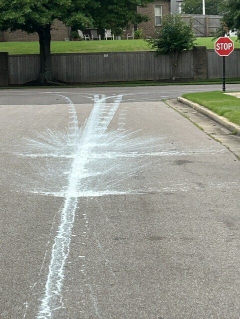 Picture of light blue paint splatters and tracks on a road leading to a stop sign, then right and left on adjacent road.