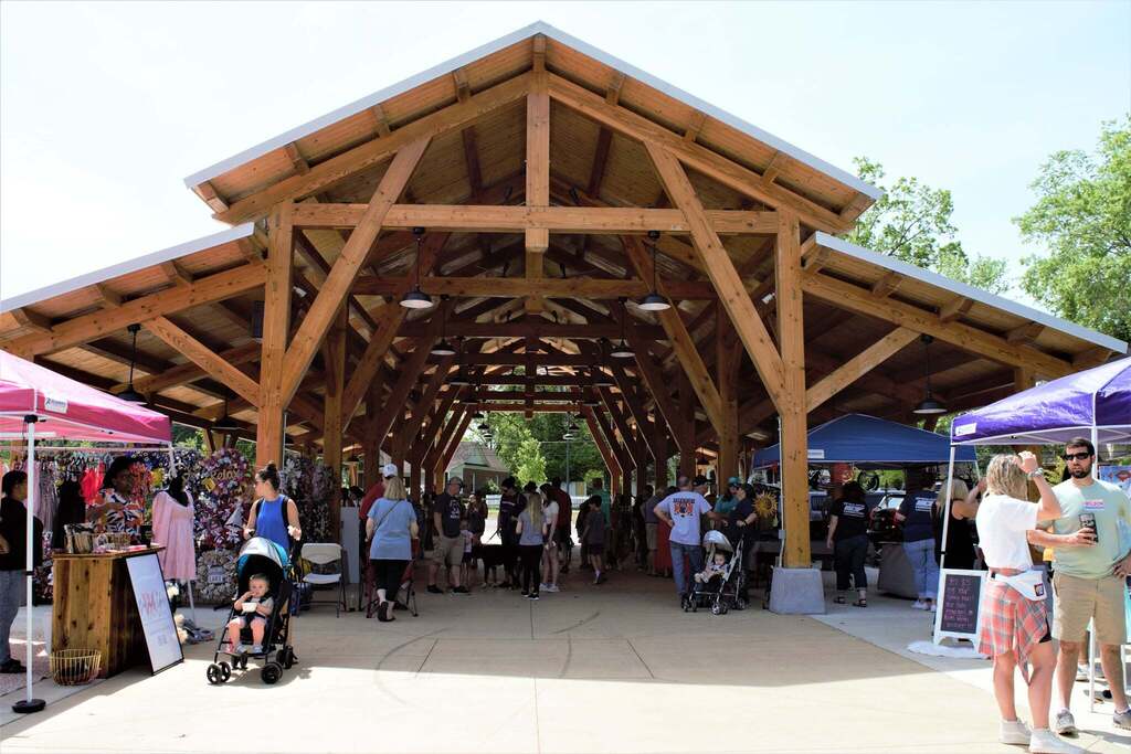 Picture of a bunch of vendors at a market underneath a tall wooden pavilion