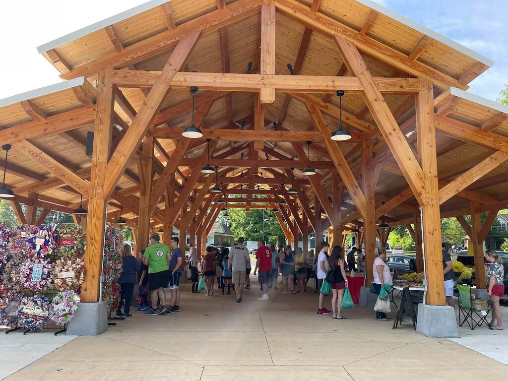 Wooden market pavilion with vendors and shoppers milling around underneath