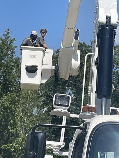 Photo of two men in a white bucket at end of the arm of a bucket truck