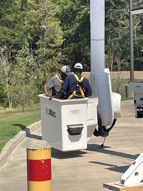 Photo of two men in safety harnesses in the white bucket of a bucket truck, staring at the controls and hovering about a foot off the ground
