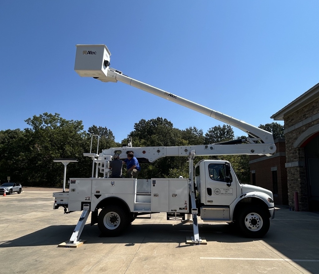 Photo of a white bucket truck parked with its stabilizers out and the arm partially extended up into the air with an empty bucket
