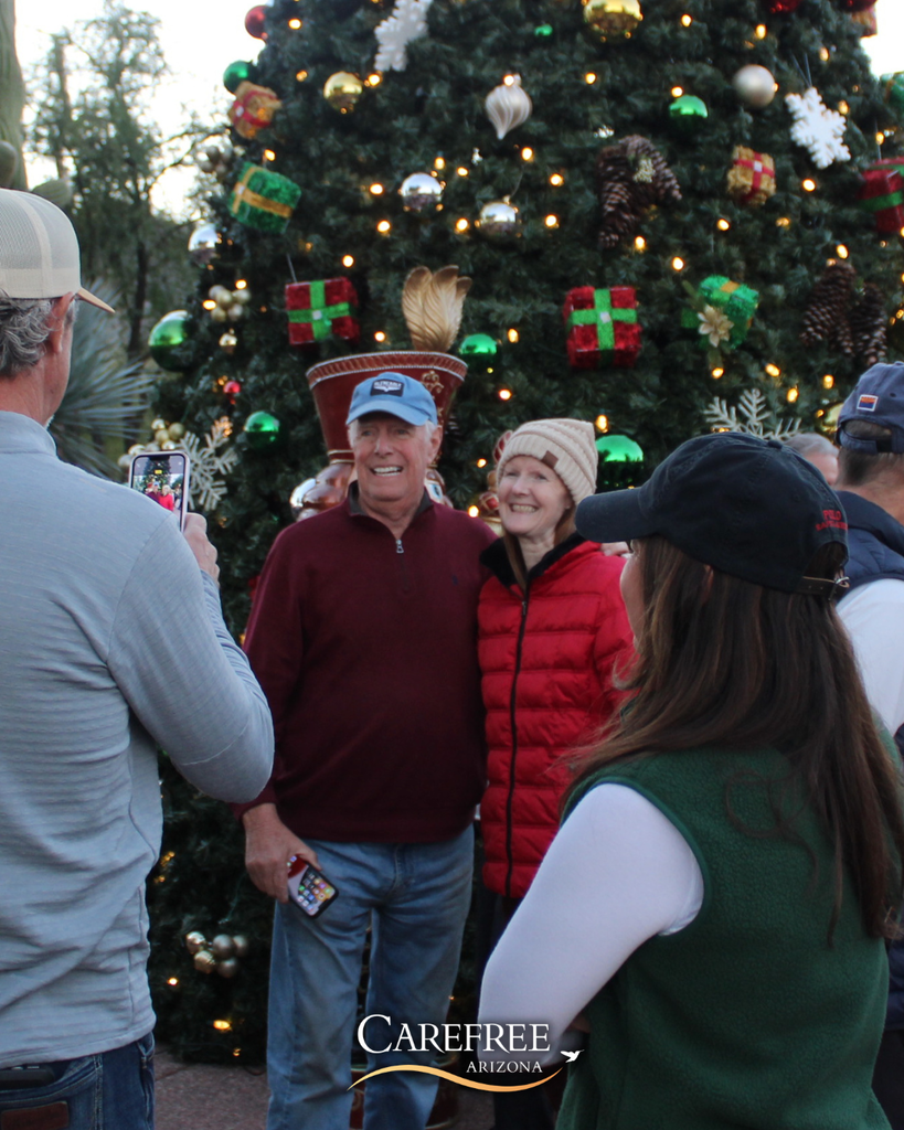 People smiling and getting their photo taken in front of a Christmas tree