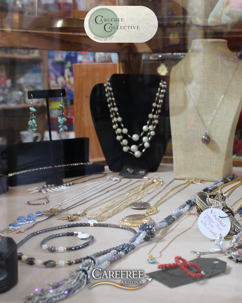 Display of handcrafted necklaces, bracelets, and earrings arranged on stands and flat surfaces in a jewelry store window.