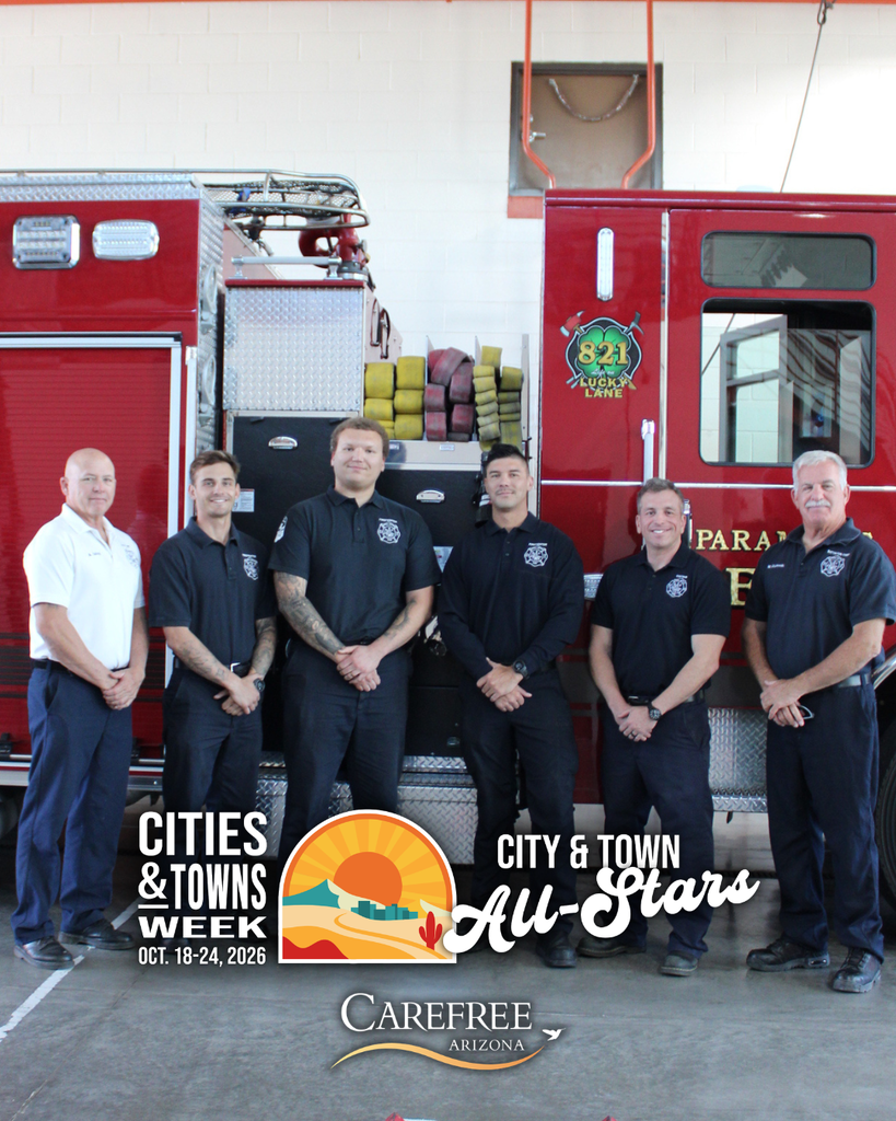 Six Carefree Fire Department and Rural Metro Fire personnel stand in front of a red fire truck at the fire station.