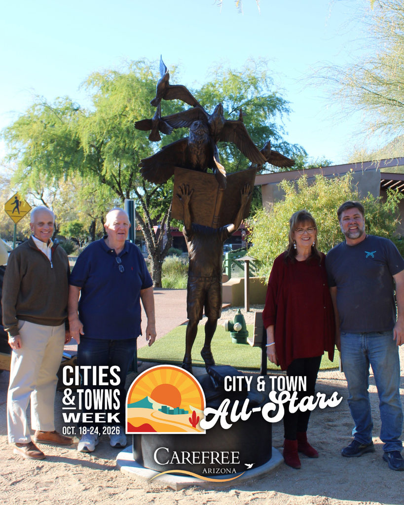 Four community members stand beside a bronze sculpture featuring birds and an open book in Carefree.