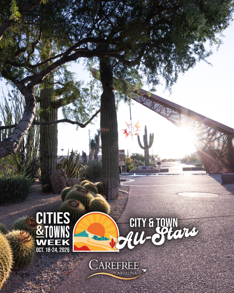A scenic walkway through the Carefree Desert Gardens features towering cacti, desert landscaping, and sunlight filtering through the trees.