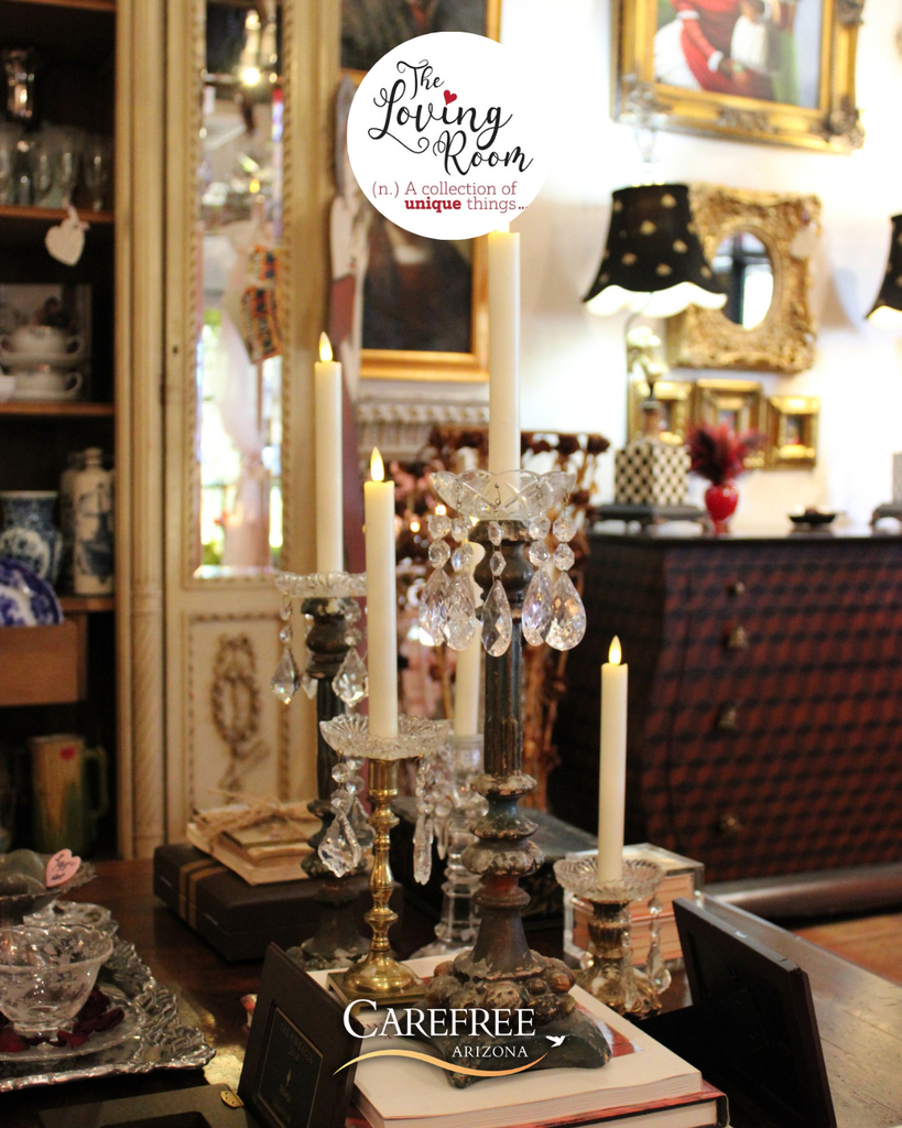 Elegant crystal and brass candle holders with lit candles displayed on a wooden table in a vintage-style room filled with ornate mirrors and antique decor.