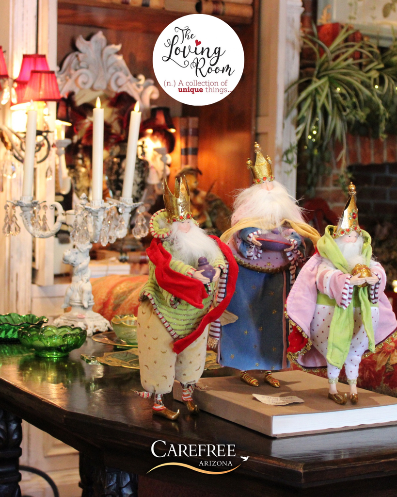 Three whimsical king figurines dressed in colorful robes and crowns displayed on a wooden table in a cozy, vintage-style room.