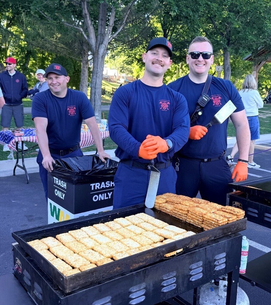 firefighters cooking hash browns on a flattop grill outside with trees in the background