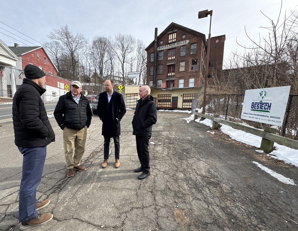 Four men speaking in front of an old mill