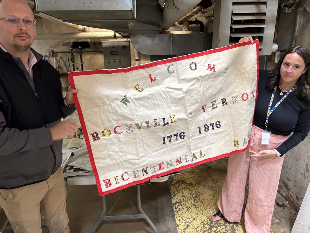 Town Administrator and Northeast Principal hold a bicentennial banner