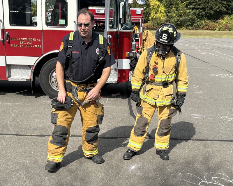 Firefighter Joe Hampton, left, talks to students as Firefighter Adam Bycholski shows students the protective gear firefighters wear