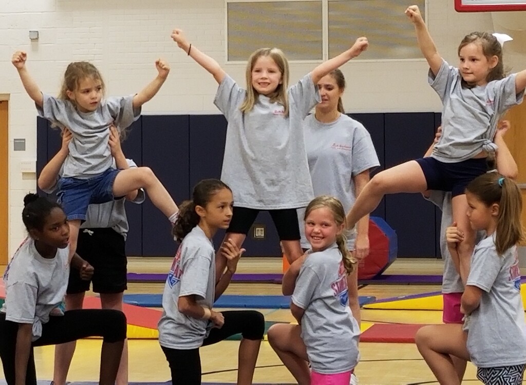 Children in a cheer pose with tumbling mats in the background.