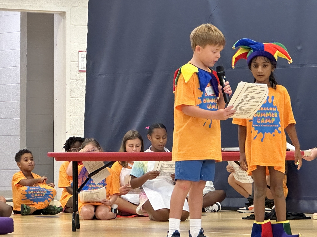 Two children in jester costumes reading a script with a microphone.