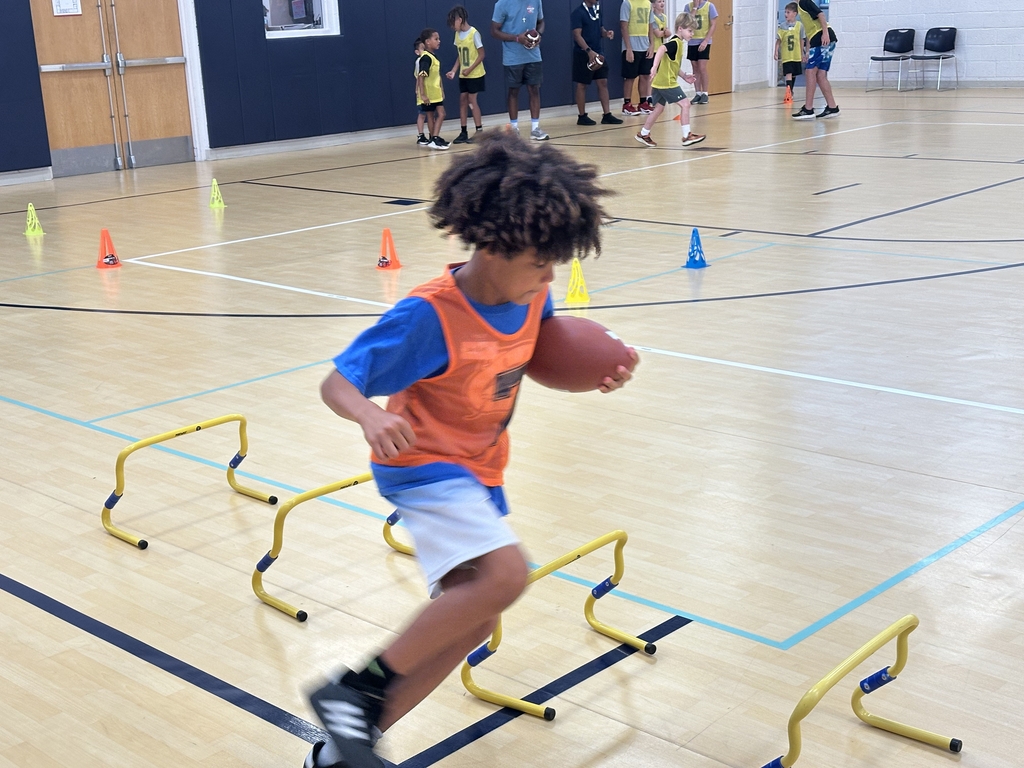 Child running with a football at flag football camp.