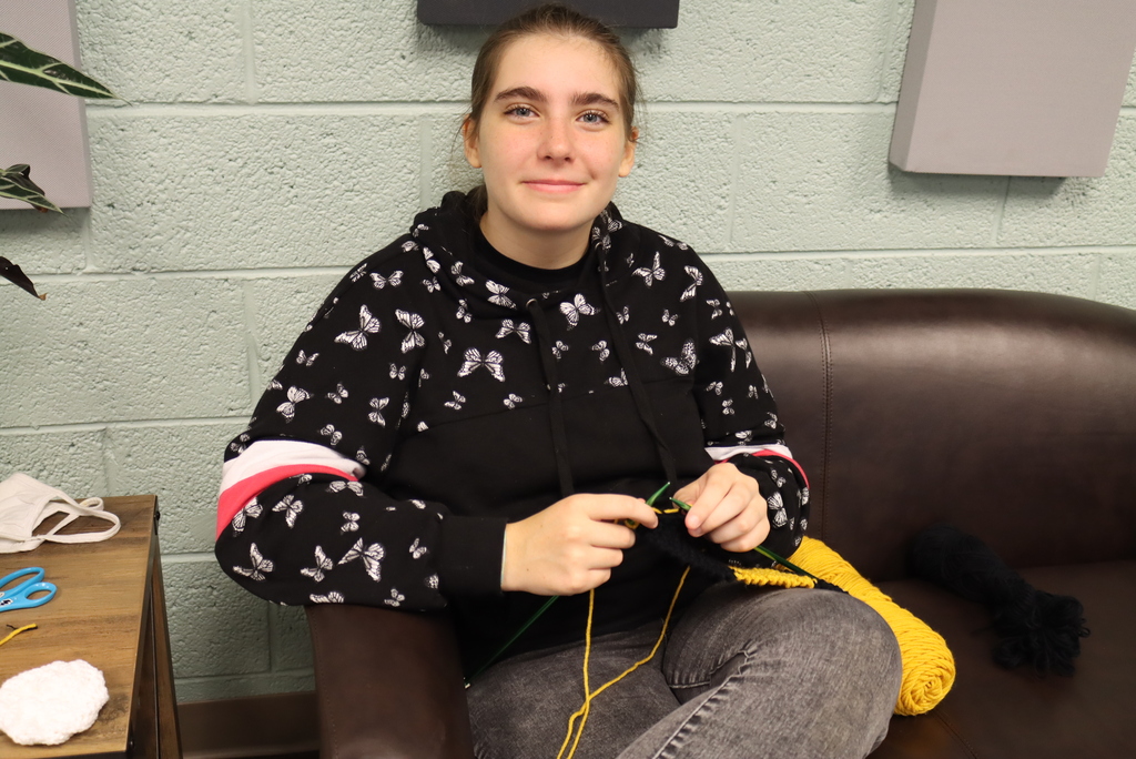 Girl knitting and smiling at camera while sitting in a couch