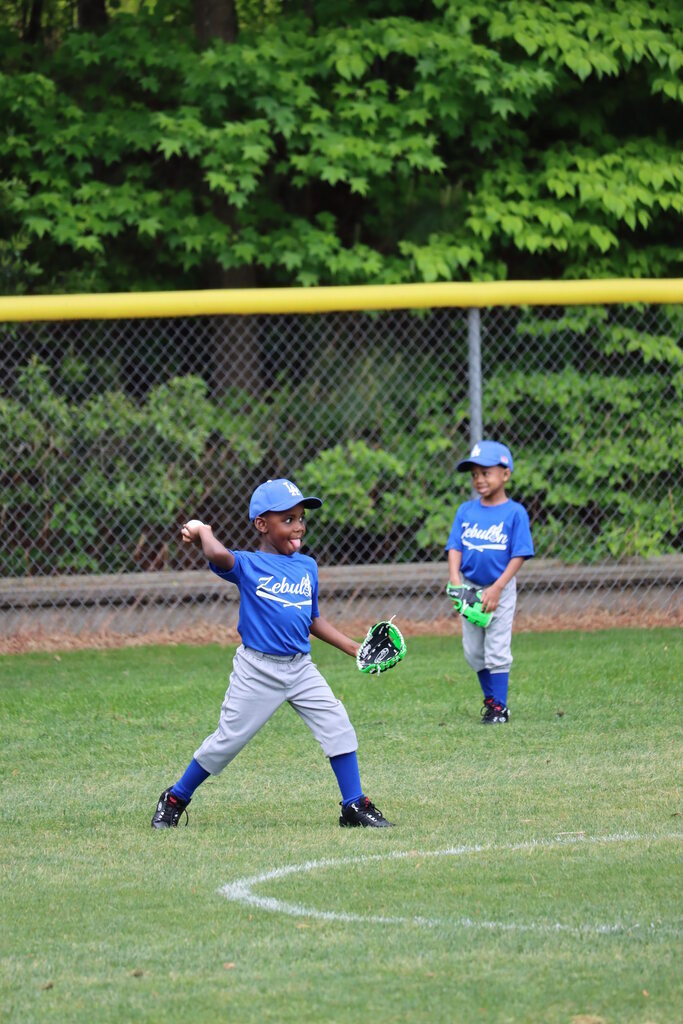 A child in a baseball uniform throwing the ball while sticking his tongue out