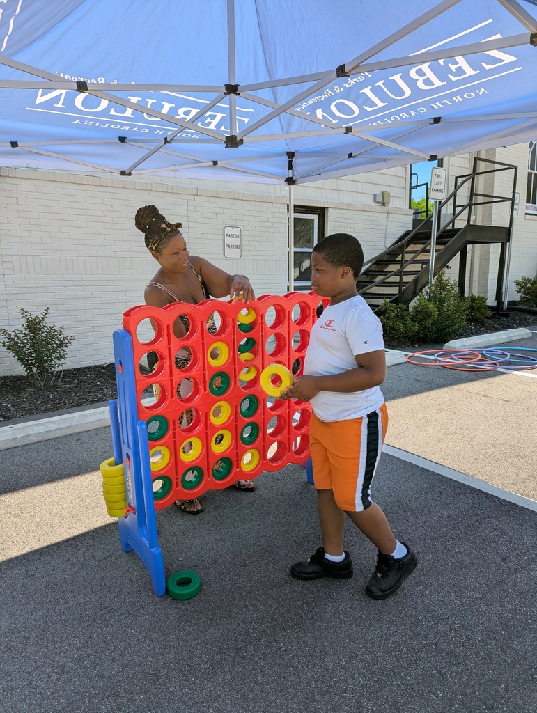 A woman and child playing giant connect 4 outside under a tent.