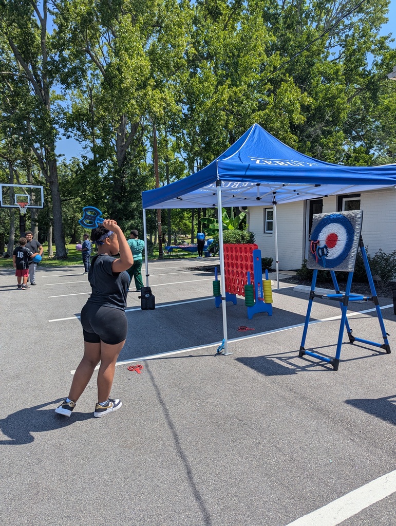 Girl playing with an axe throwing game while more children play basketball in the background.