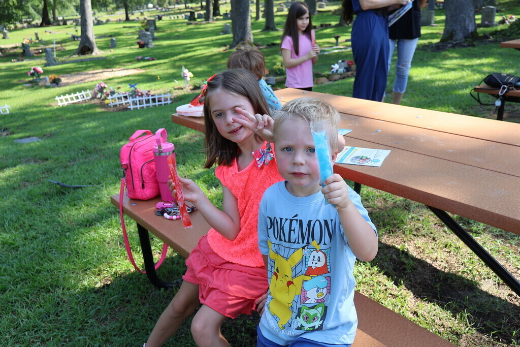 A boy and a girl posing for the camera with their popsicles at a picnic table