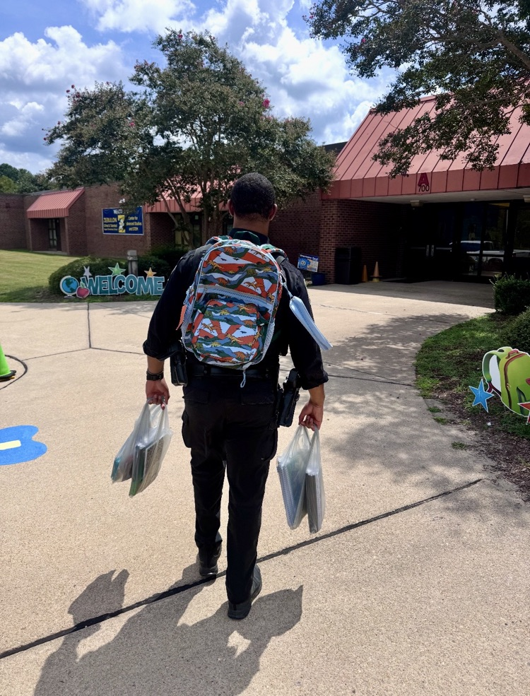an officer carrying a bag of school supplies with a bookbag into a school