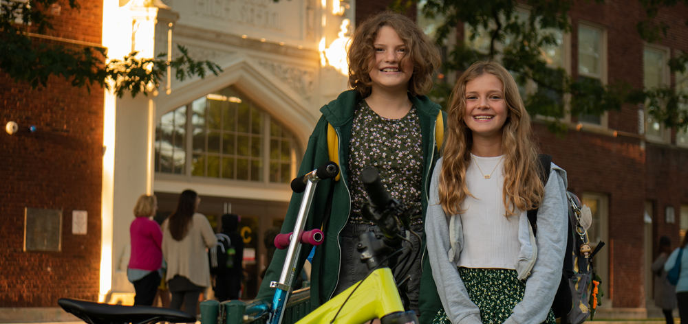 image of two girls standing beside each other smiling in front of a school.