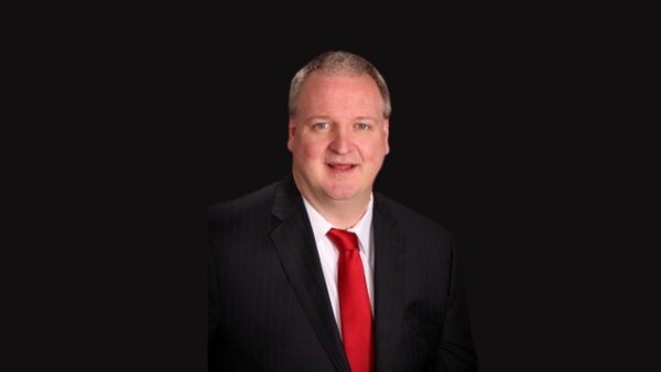 image of man smiling at camera posing for photo with red tie and black suit with black background.