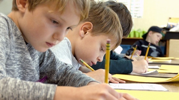 image of students writing on yellow paper at their desks looking down at the paper