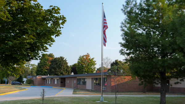 image of American flag and flag pole in front of brick building surrounded by trees