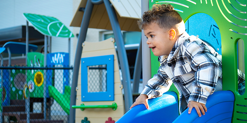 Young student smiling while going down slide on playground
